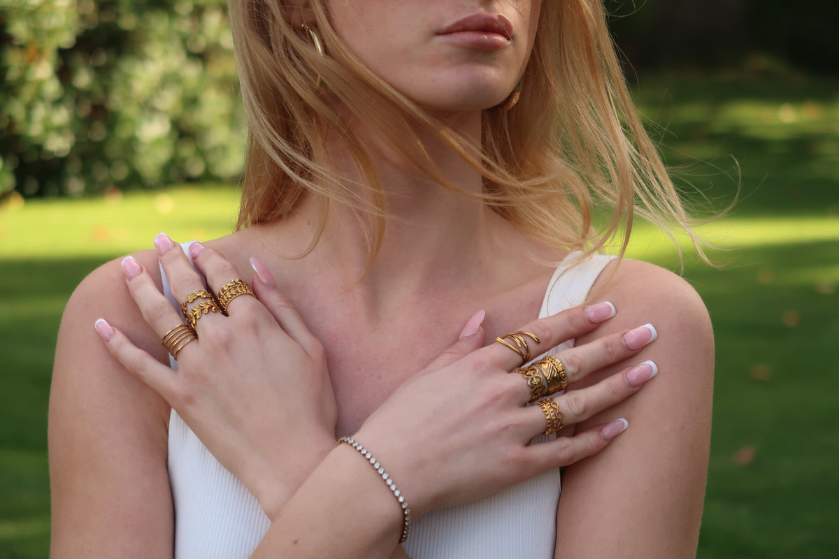 Woman with crossed hands wearing stacked gold AMORA rings and a tennis bracelet